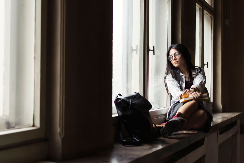 Woman sitting by window looking out with book bag by feet Trellis Strategies